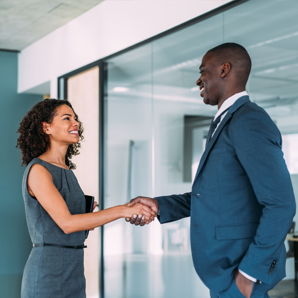 Young man being greeted by and shaking hands with woman in office setting.