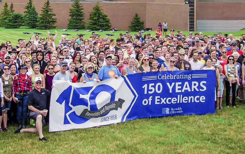 Image of large group of Reynolds employees outside the headquarters, holding a 150 Years sign.